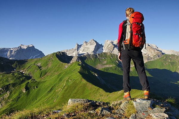 Person mit Rucksack auf dem Rücken steht auf Berggipfel